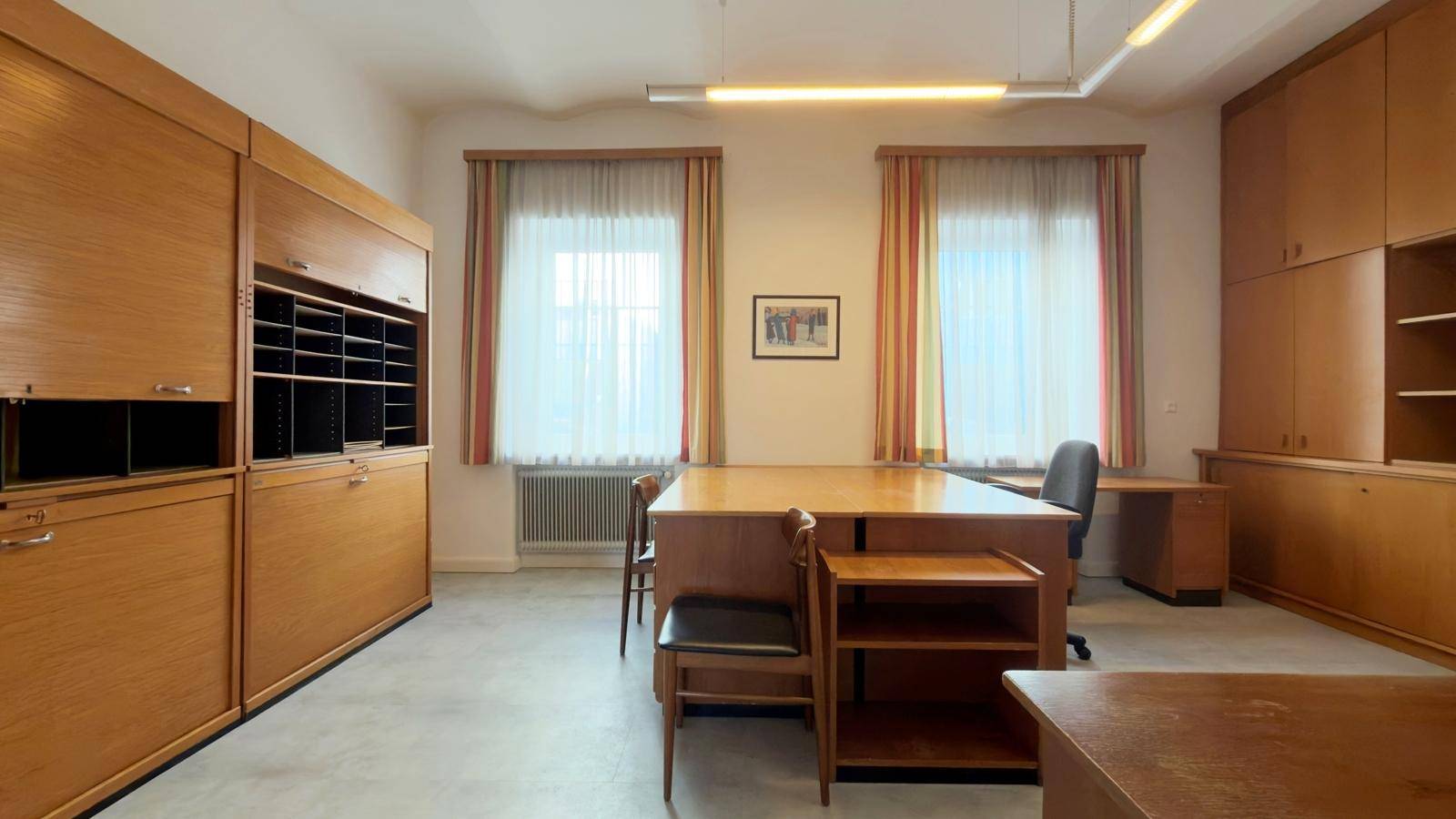 Geräumiges Büro mit mehreren Schreibtischen, Holzschränken und großen Fenstern für viel Tageslicht.