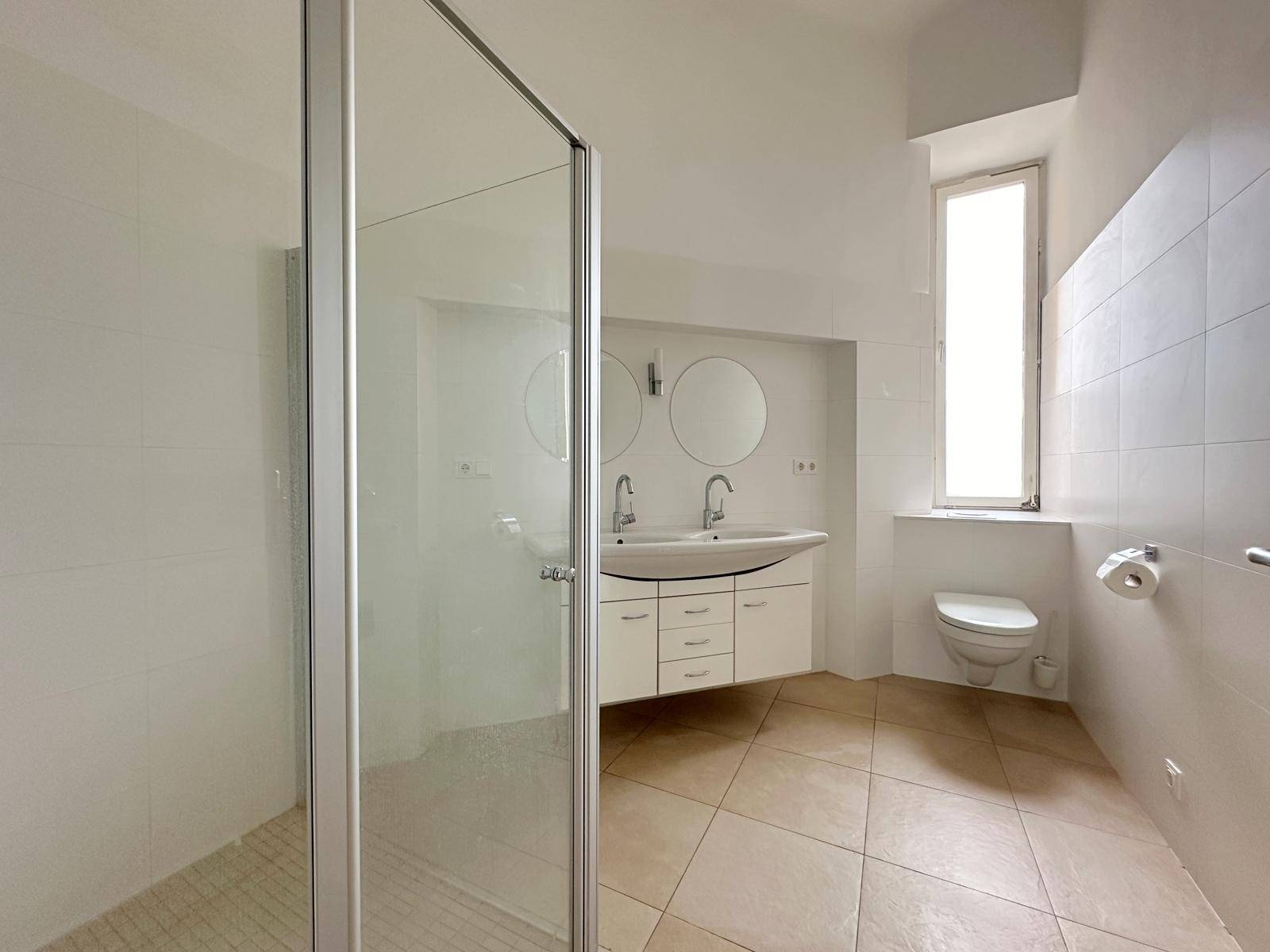 Modernes Badezimmer mit Doppelwaschbecken, großer Duschkabine und hellem Fliesenboden.