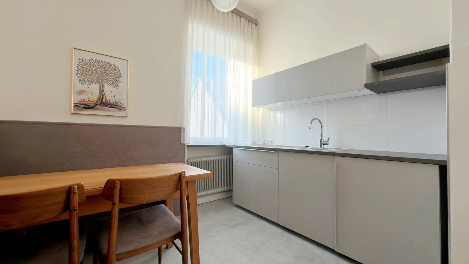 Moderne Küchenzeile mit grauen Schränken, Spüle und einem kleinen Essbereich am Fenster.