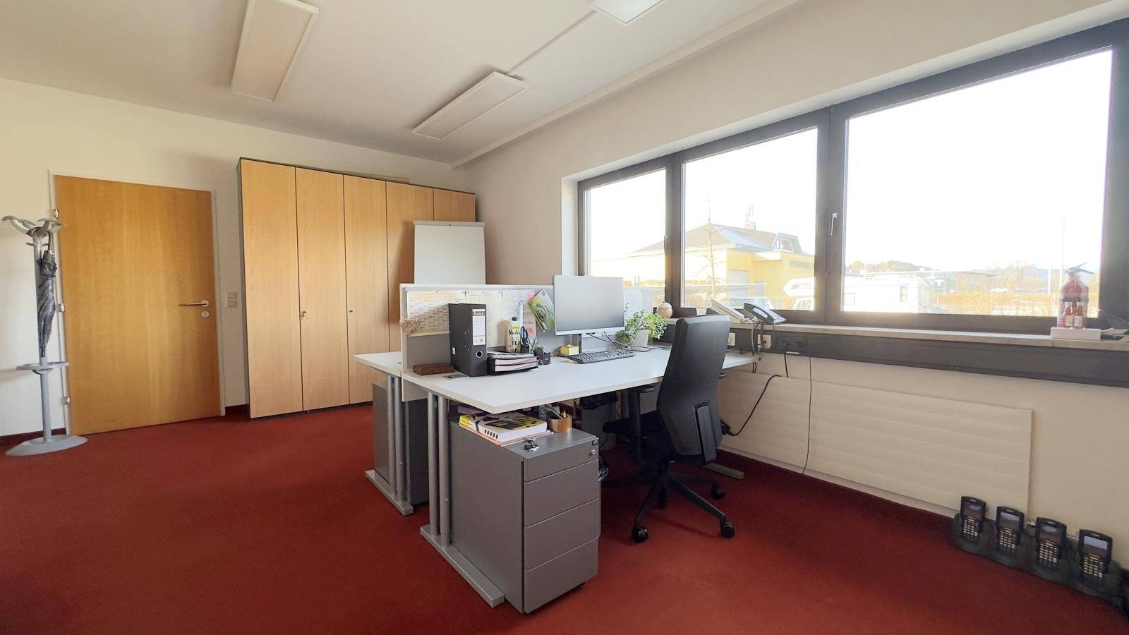 Geräumiges Büro mit großem Fenster, Schreibtisch, Bürostuhl und integrierten Holzschränken für Stauraum.
