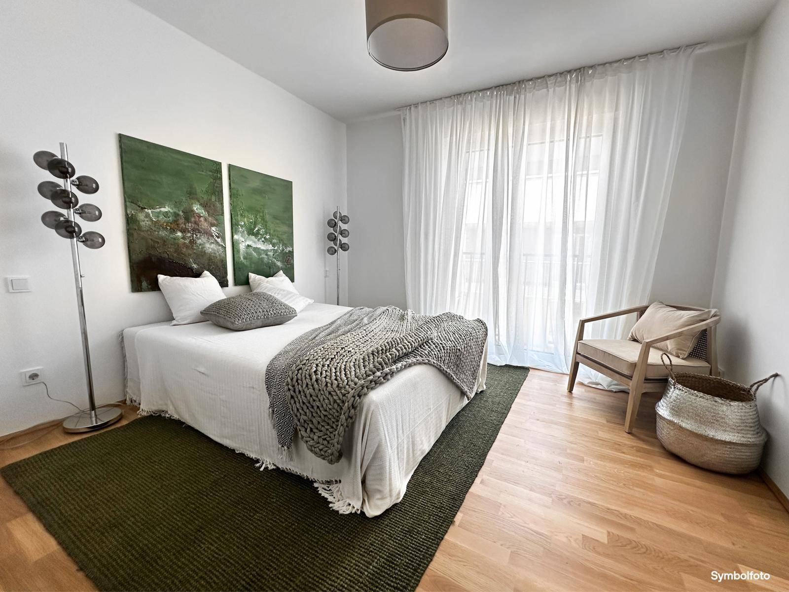 Helles Schlafzimmer mit Holzboden, gemütlichem Bett und großen Fenstern mit transparenten Vorhängen.