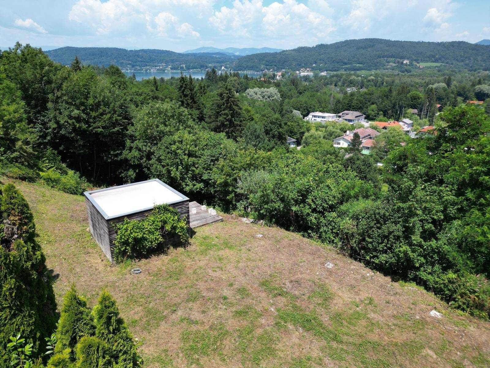Luftaufnahme eines Grundstücks mit kleinem Schuppen, umgeben von Bäumen und mit Seeblick.