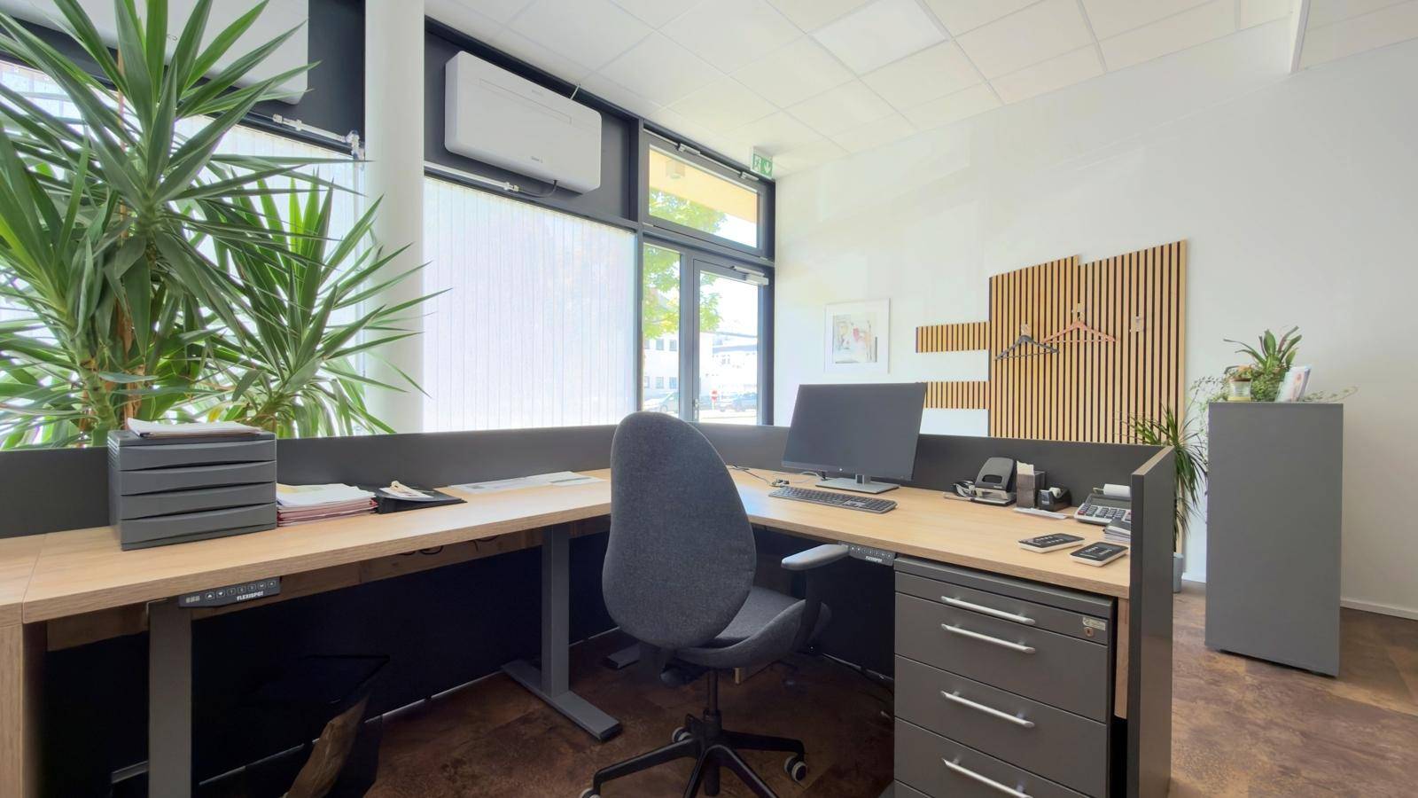Detailansicht eines modernen Arbeitsplatzes mit Schreibtisch, Bürostuhl und großen Fenstern.