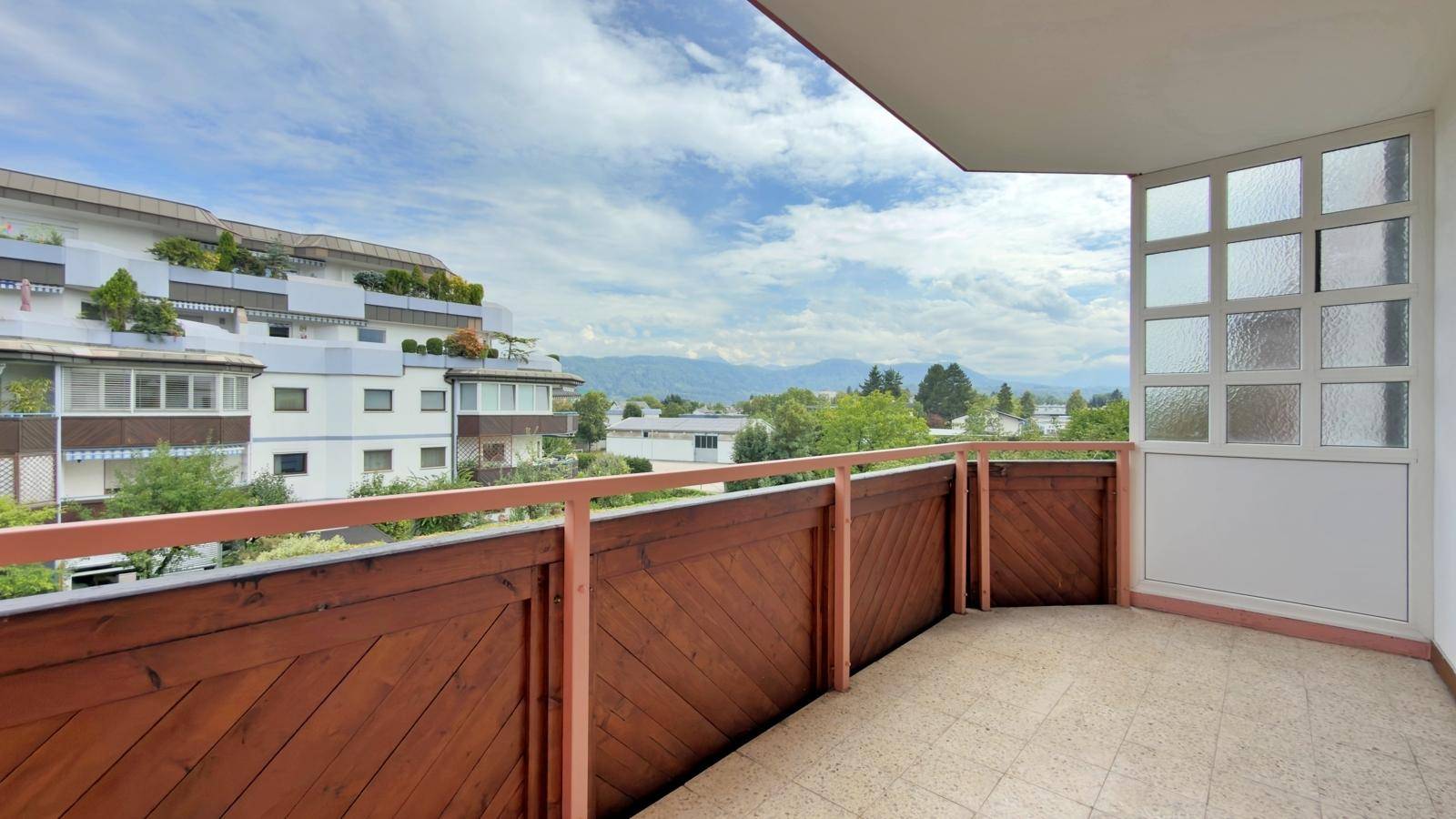 Heller Balkon mit Holzelementen und Panoramablick auf die grüne Umgebung und die Berge.