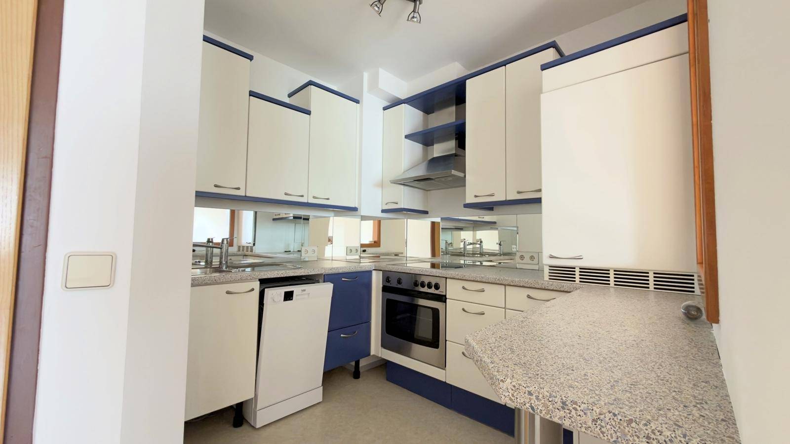 Funktionale Küche mit blauen und weißen Schränken, integrierten Geräten und Spülmaschine.