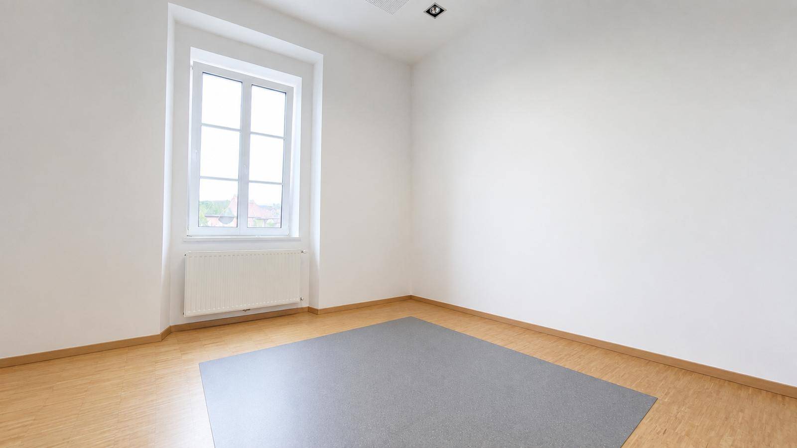 Heller, leerer Raum mit weiß gestrichenen Wänden, Holzfußboden und einem Fenster für natürliches Licht.