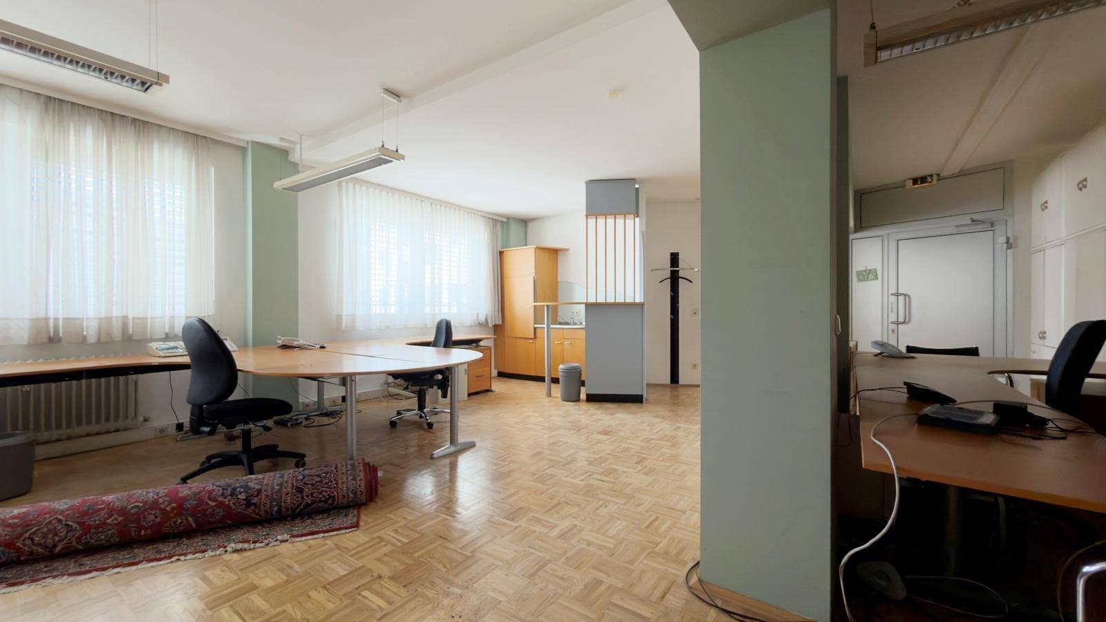 Großzügiger Bürobereich mit Fischgrätparkett und mehreren Arbeitsplätzen, bietet eine helle und offene Atmosphäre.