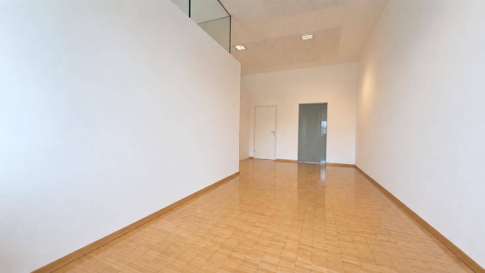 Geräumiger, heller Raum mit Holzfußboden, weißen Wänden und zwei Türen, die zu weiteren Bereichen führen.