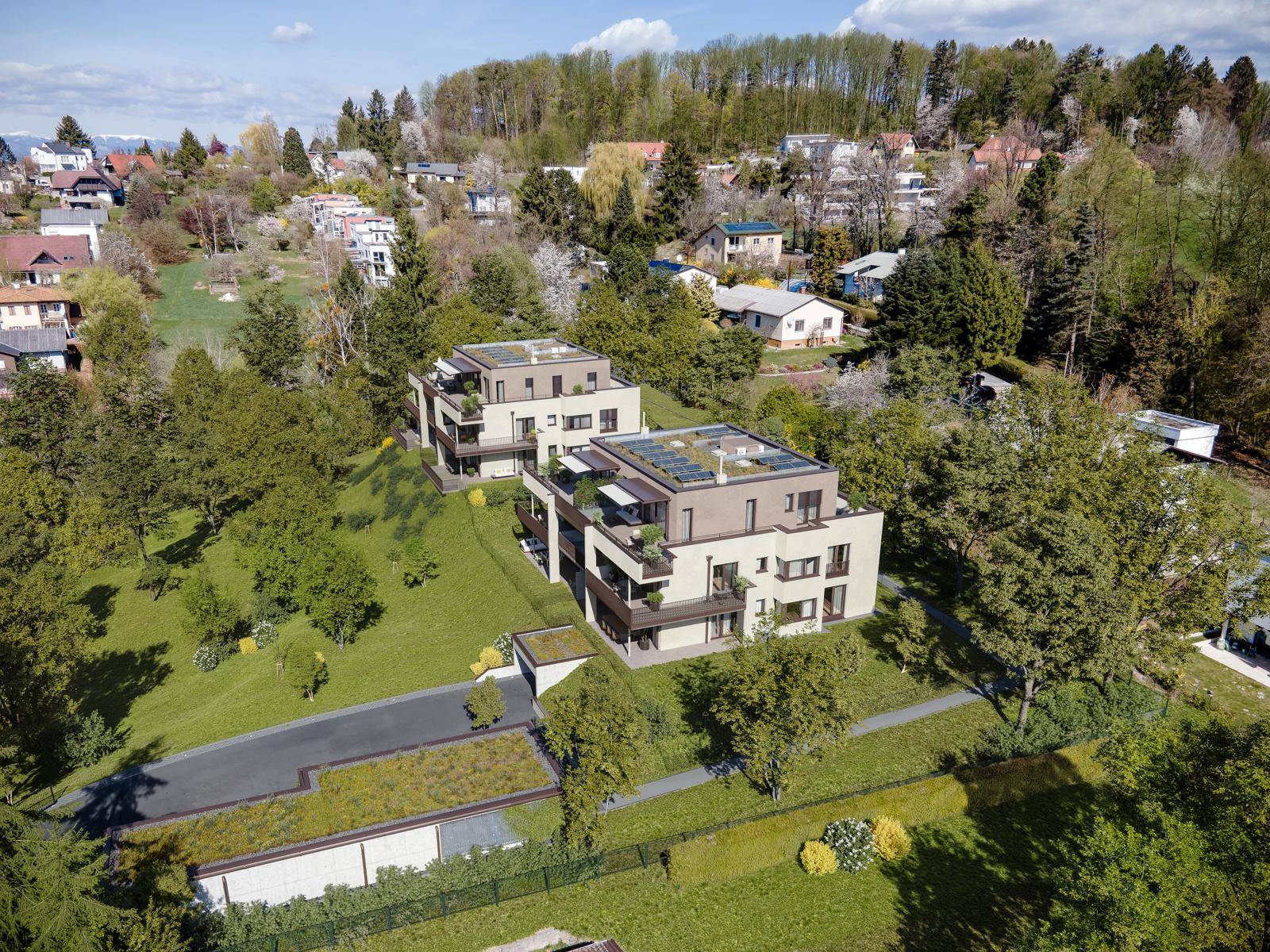 Luftaufnahme von zwei modernen Wohngebäuden in grüner Umgebung mit Photovoltaikanlagen auf den Dächern.