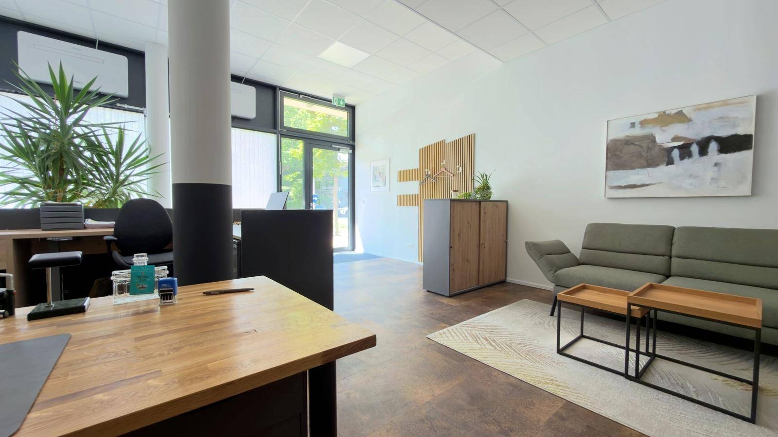 Freundliches Büro mit modernen Arbeitsplätzen, einer Garderobe und einem bequemen Sofa.