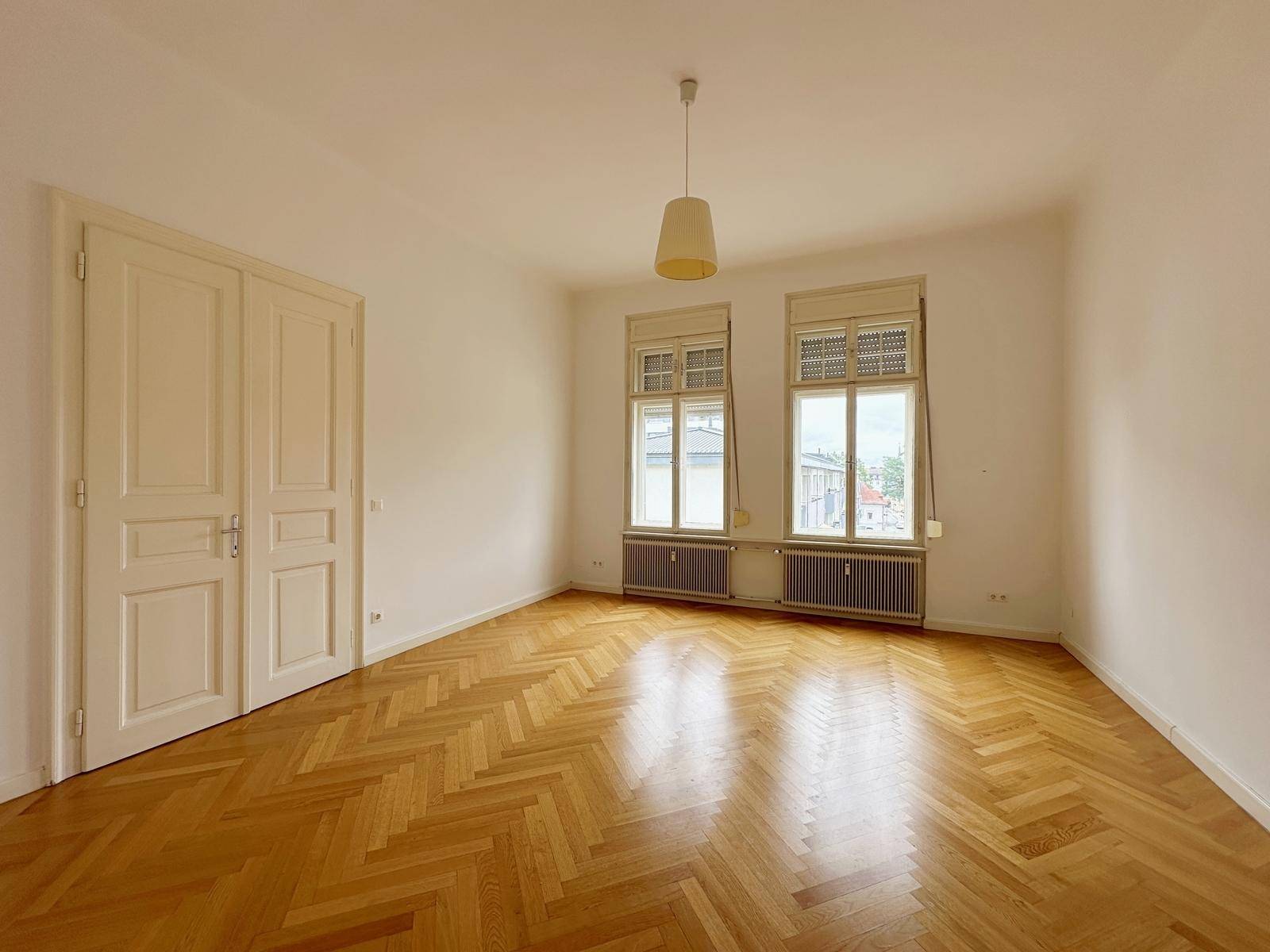 Leerer Raum mit Fischgrätparkett, hohen Decken und Doppeltüren, ideal als Esszimmer.