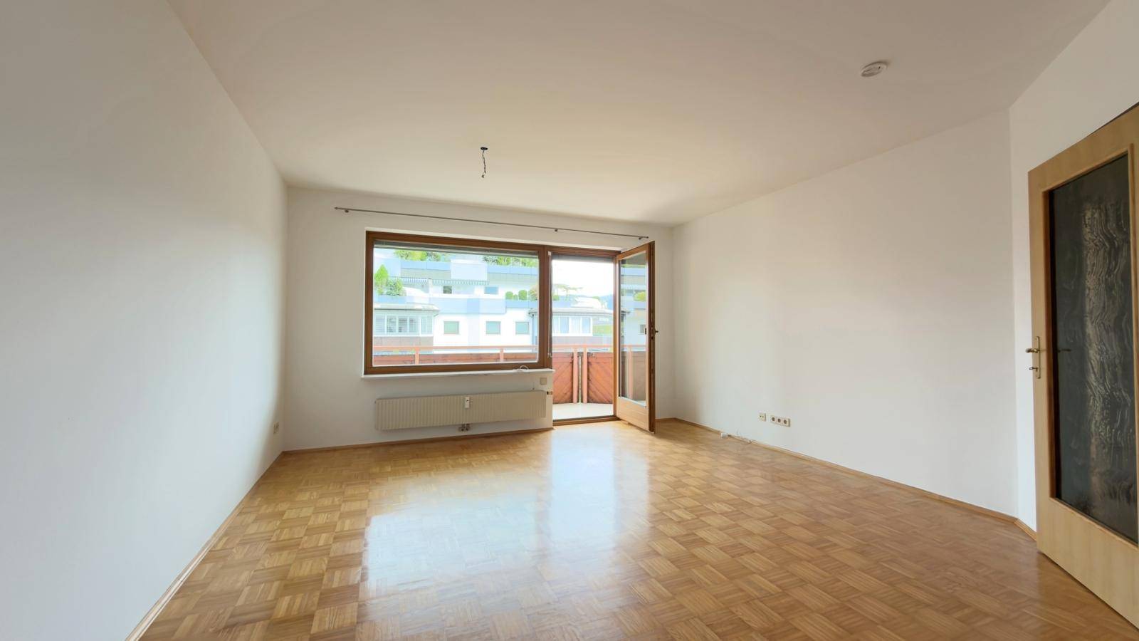 Geräumiges Wohnzimmer mit hellem Parkettboden und Fensterfront zum Balkon.
