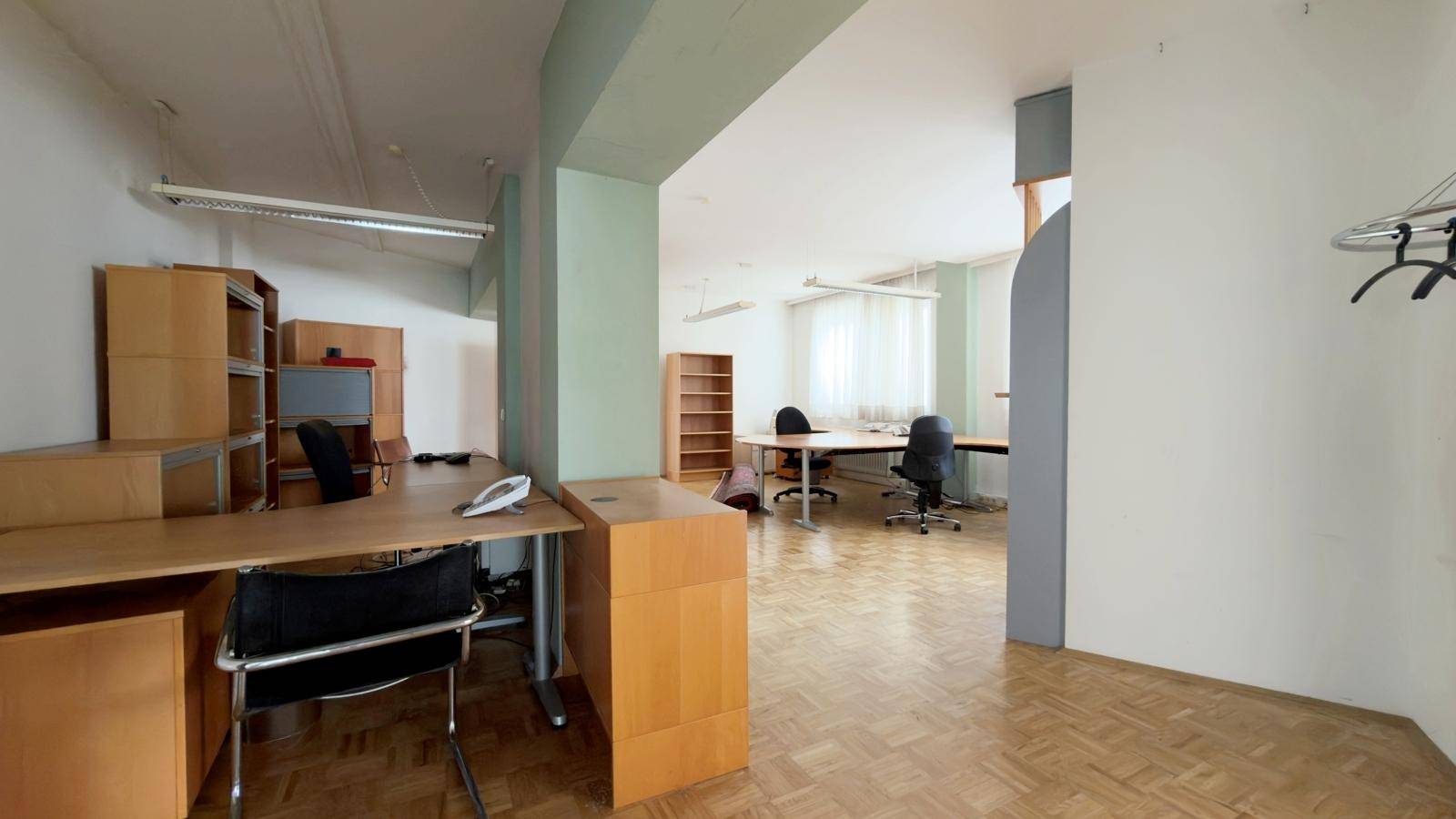 Offener Bürobereich mit Holzmöbeln und Fischgrätparkett, bietet flexible Arbeitsplätze und viel Raum.