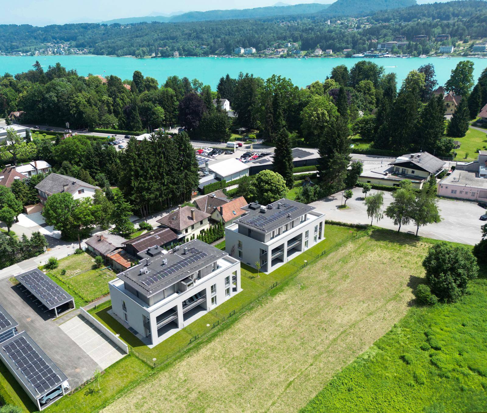 Luftaufnahme von zwei modernen Wohngebäuden mit Seeblick, umgeben von Natur und Photovoltaikanlagen.