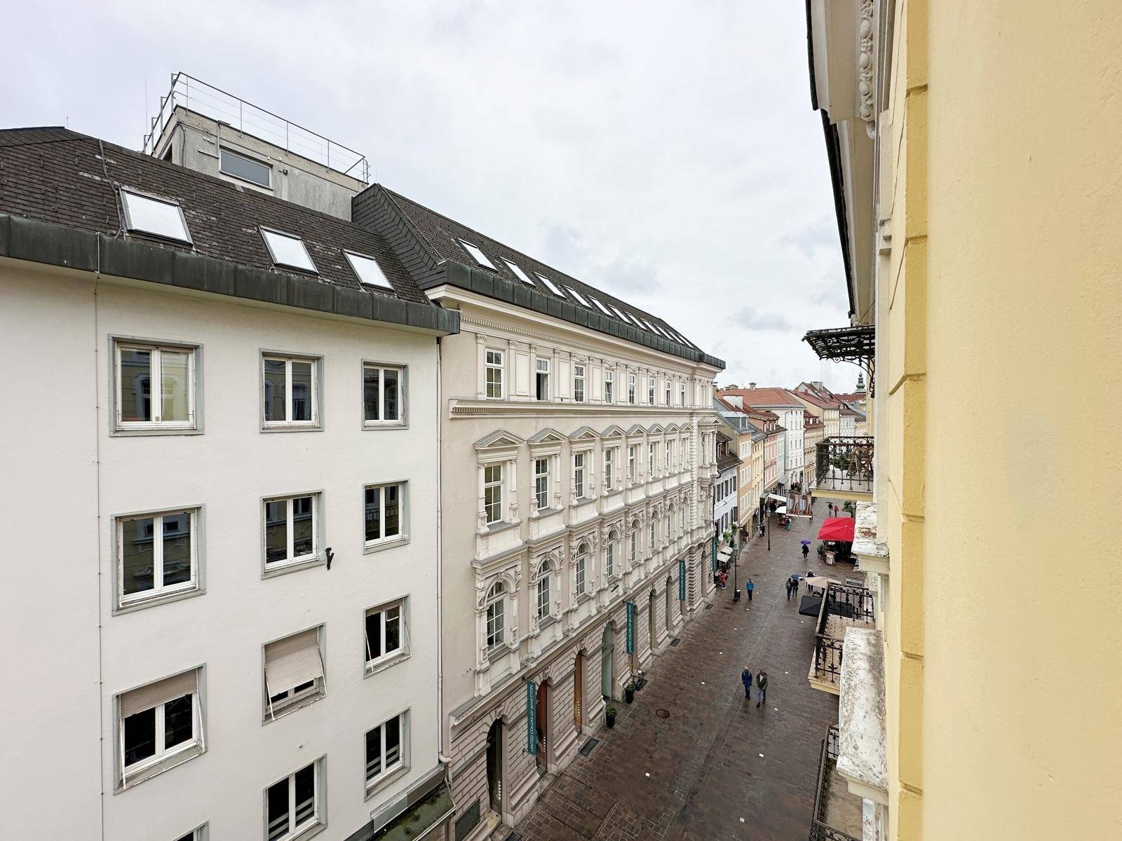 Blick auf eine belebte Straße mit historischen Gebäuden und Geschäften unter bewölktem Himmel.