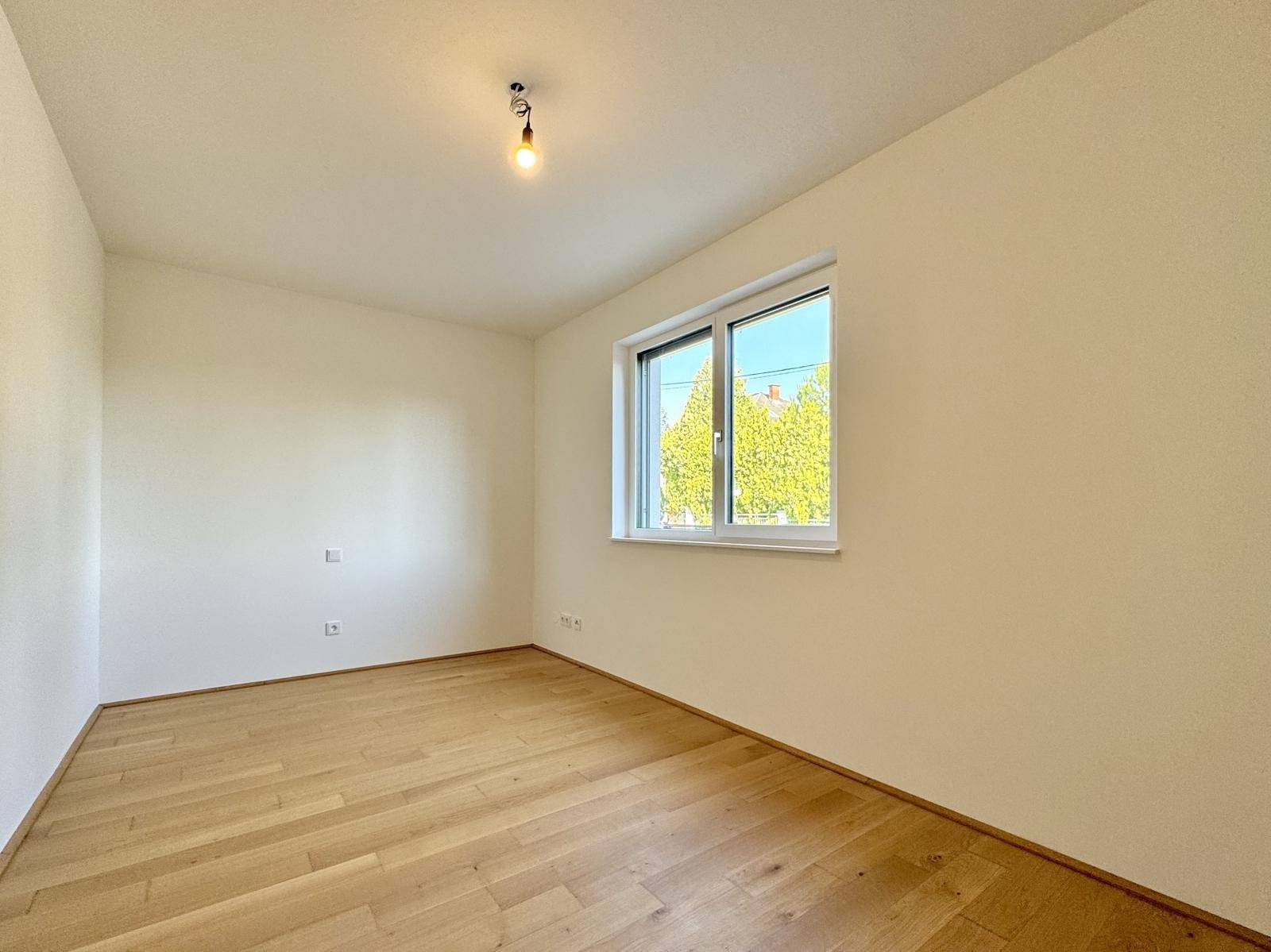 Ruhiges Schlafzimmer mit Holzboden und einem Fenster mit Blick ins Grüne.
