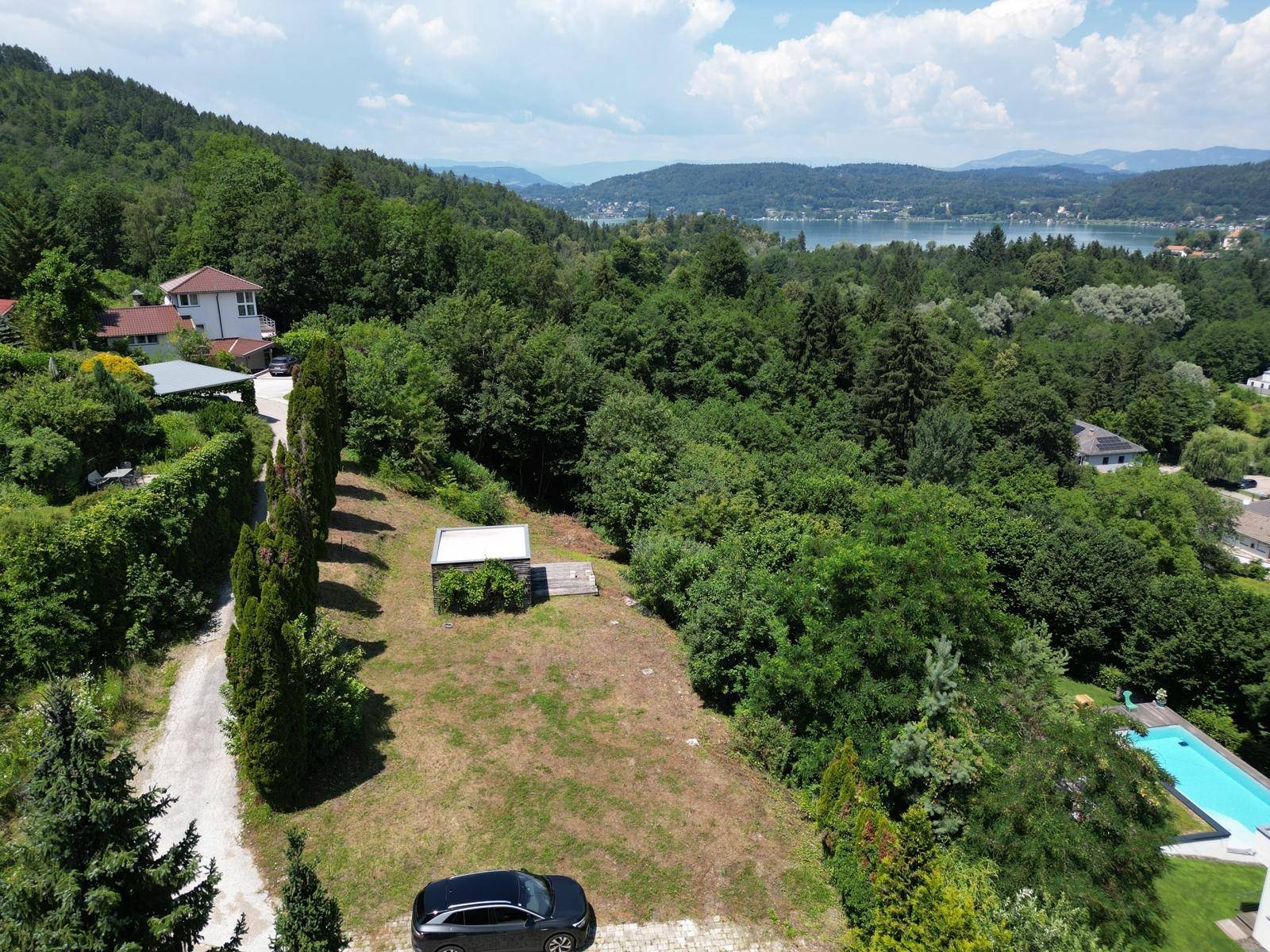 Luftaufnahme des Grundstücks mit Schuppen, angrenzendem Poolbereich und weitem Blick auf See und Berge.