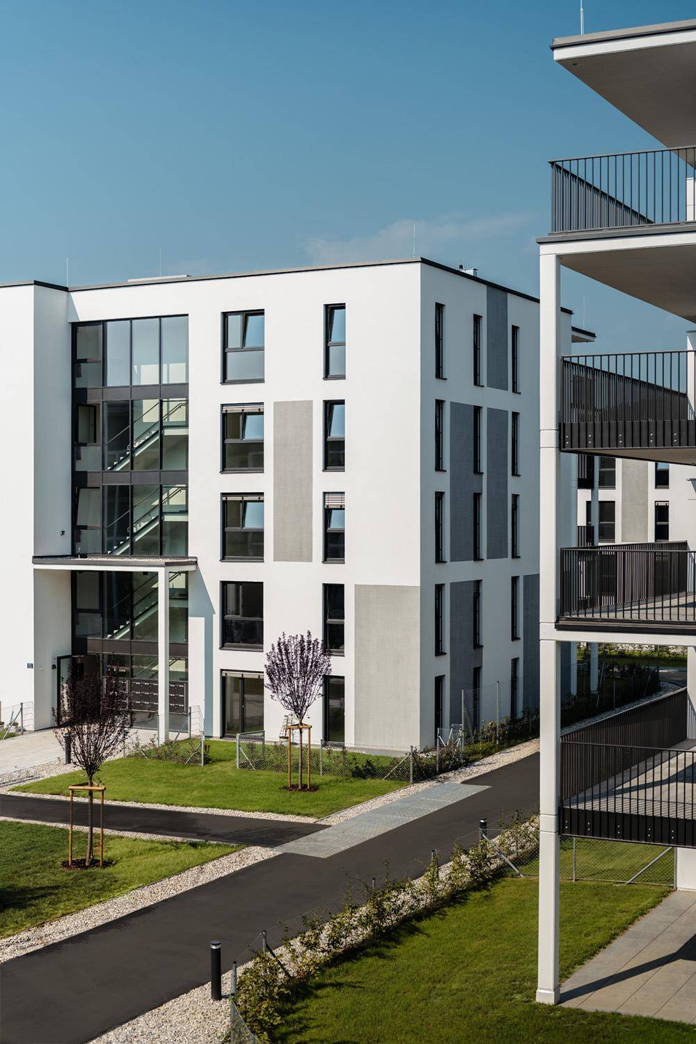 Seitenansicht eines modernen Wohngebäudes mit Balkonen, großen Glasflächen und gepflegten Wegen.