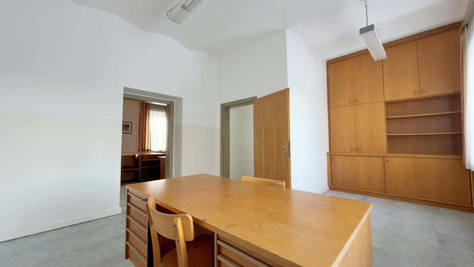 Büro mit großem Holzschreibtisch, Einbauschränken und zwei Türen zu angrenzenden Räumen.