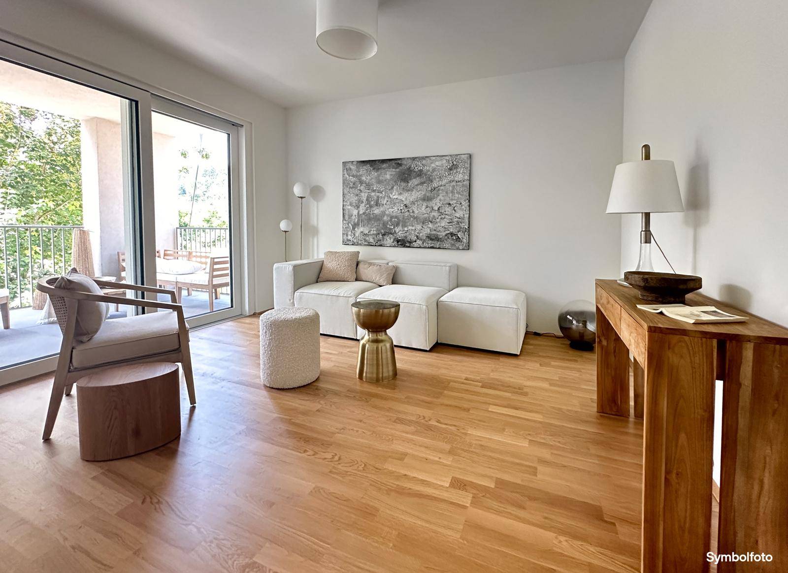 Geräumiges Wohnzimmer mit Holzboden, weißem Sofa und Zugang zu einem sonnigen Balkon.