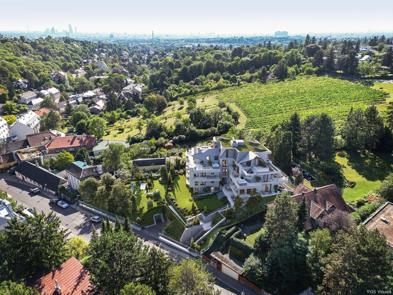 Luftaufnahme eines modernen Wohnkomplexes eingebettet in eine grüne Landschaft mit Weinbergen und Stadtblick.