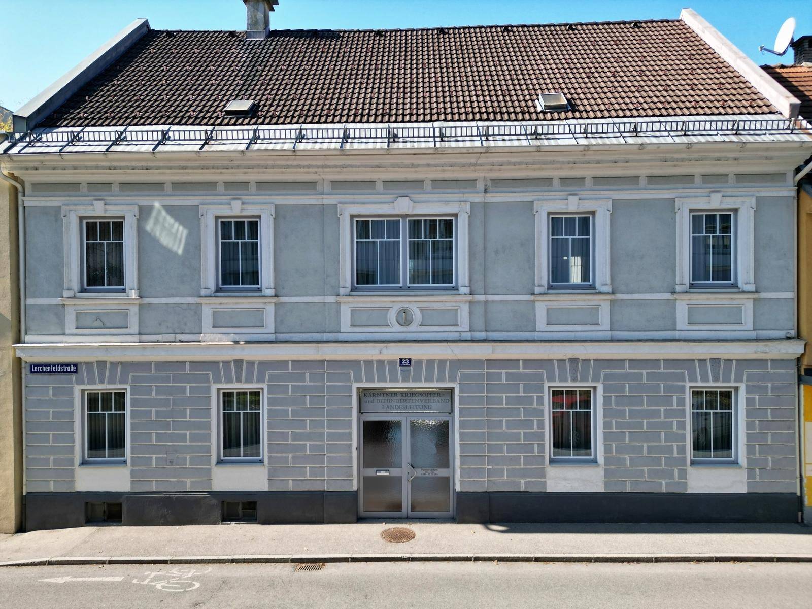 Frontansicht eines historischen Gebäudes mit symmetrischer Fassade, mehreren Fenstern und einem Eingangsbereich.