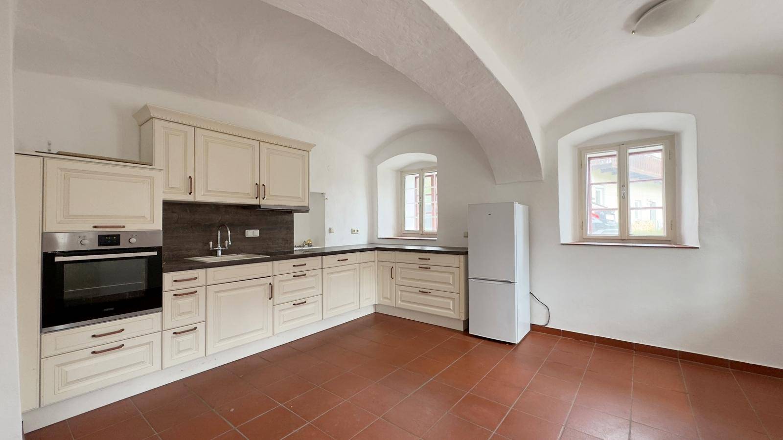 Traditionelle Küche mit cremefarbenen Einbauschränken, Backofen und Kühlschrank unter Gewölbedecken.