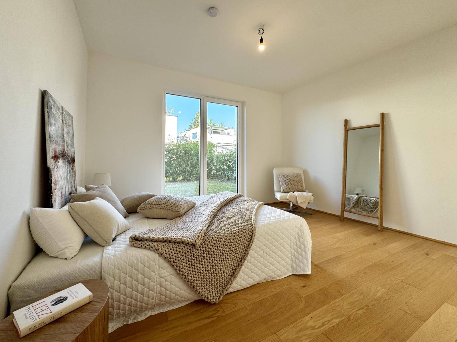 Helles Schlafzimmer mit Eichenparkett, großem Bett und bodentiefem Fenster mit Blick ins Grüne.