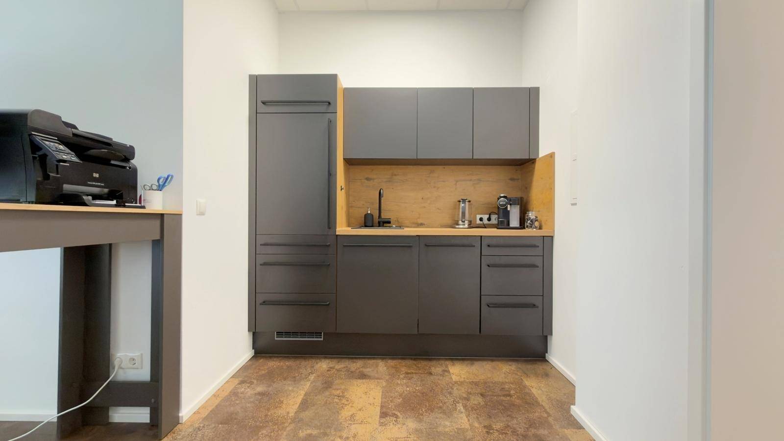 Moderne Küchenzeile in Grau und Holzoptik mit Spüle, Kühlschrank und Kaffeemaschine.