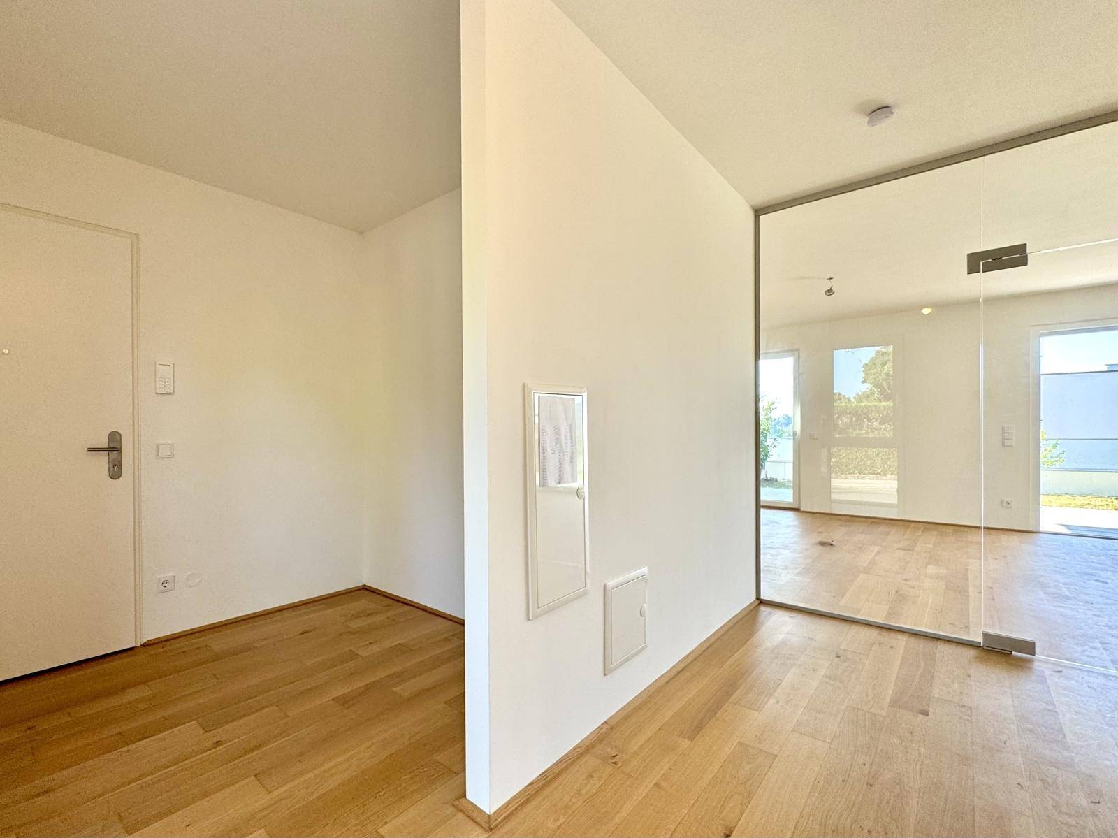Heller Eingangsbereich mit Holzboden und einer modernen Glastür zum Wohnbereich.