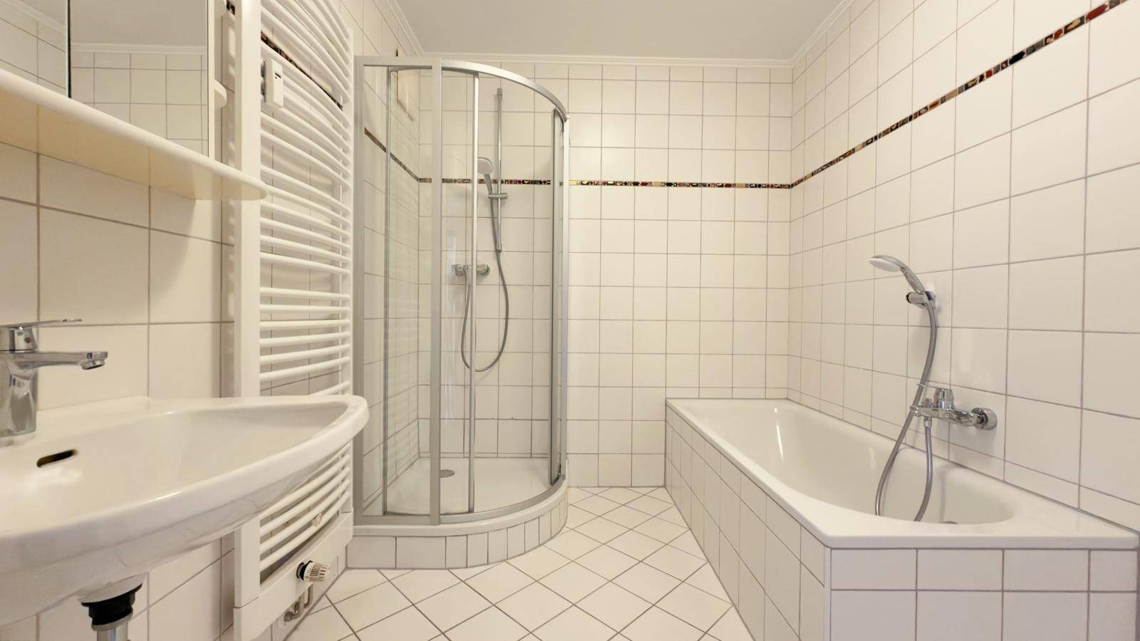 Gefliestes Badezimmer mit Badewanne, Duschkabine und Handtuchheizkörper.
