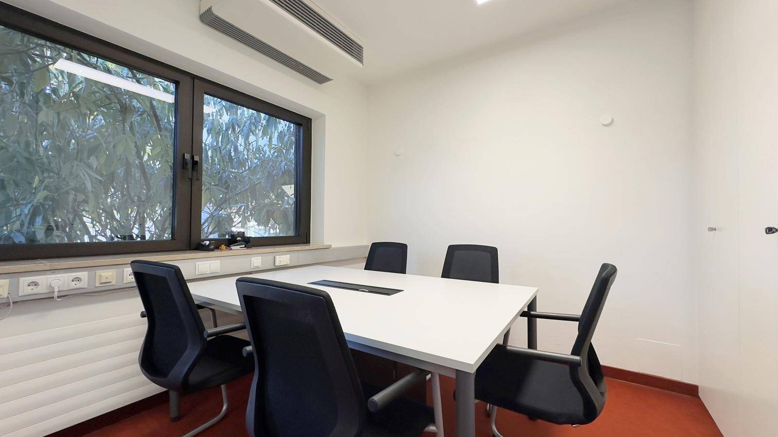 Kleiner Besprechungsraum mit Tisch, Stühlen und einem Fenster mit Blick ins Grüne.