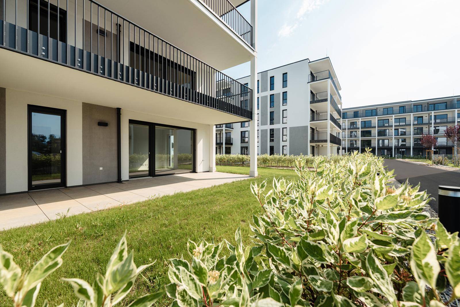 Erdgeschosswohnung mit direktem Zugang zu einer gepflasterten Terrasse und einer grünen Rasenfläche.