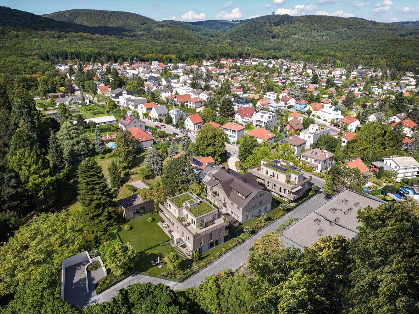 Luftaufnahme eines Wohngebiets mit modernen Gebäuden, umgeben von viel Grün und Wald.