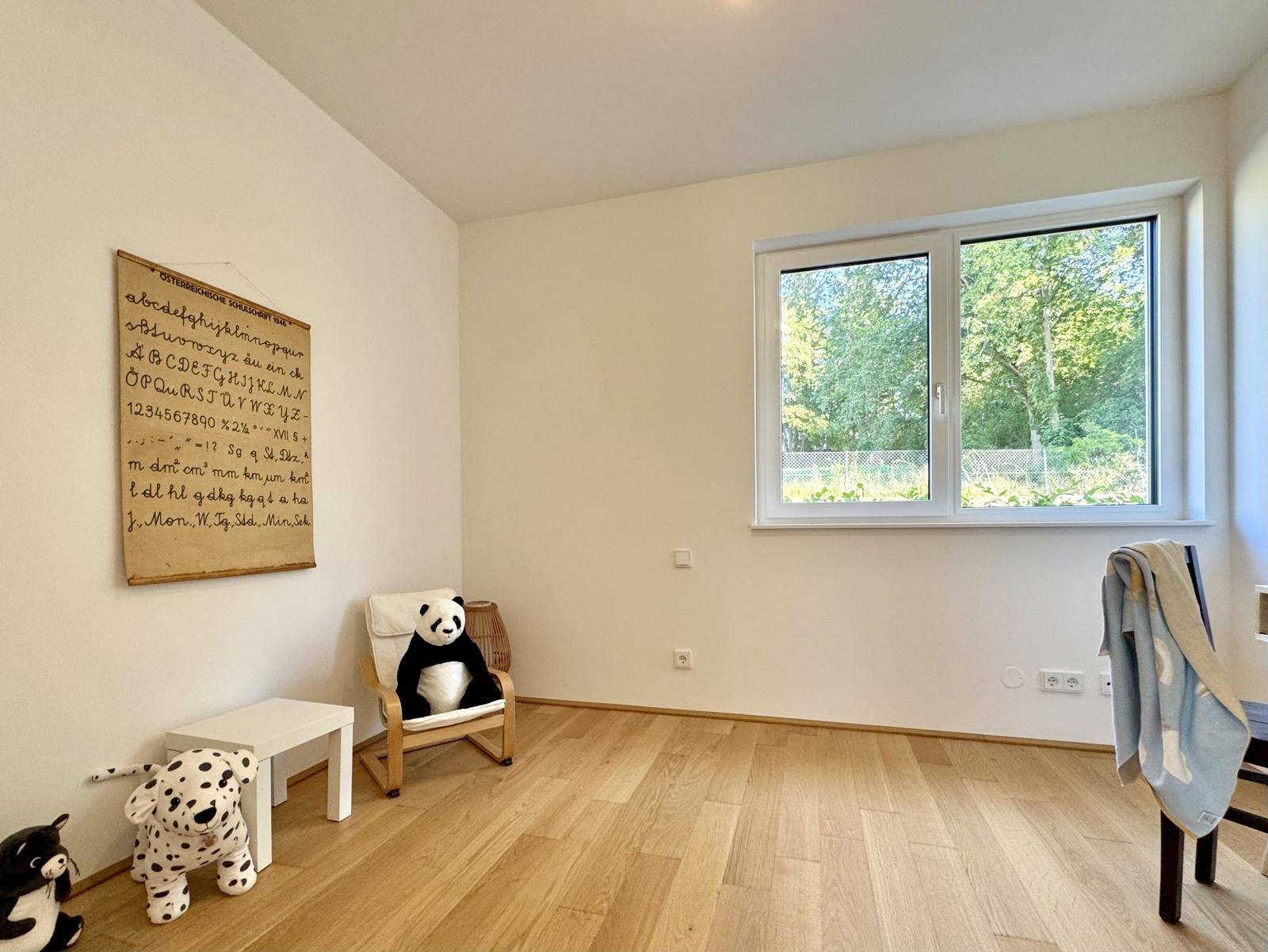 Kinderzimmer oder Gästezimmer mit Eichenparkett, hellem Fenster und einfacher, freundlicher Dekoration.