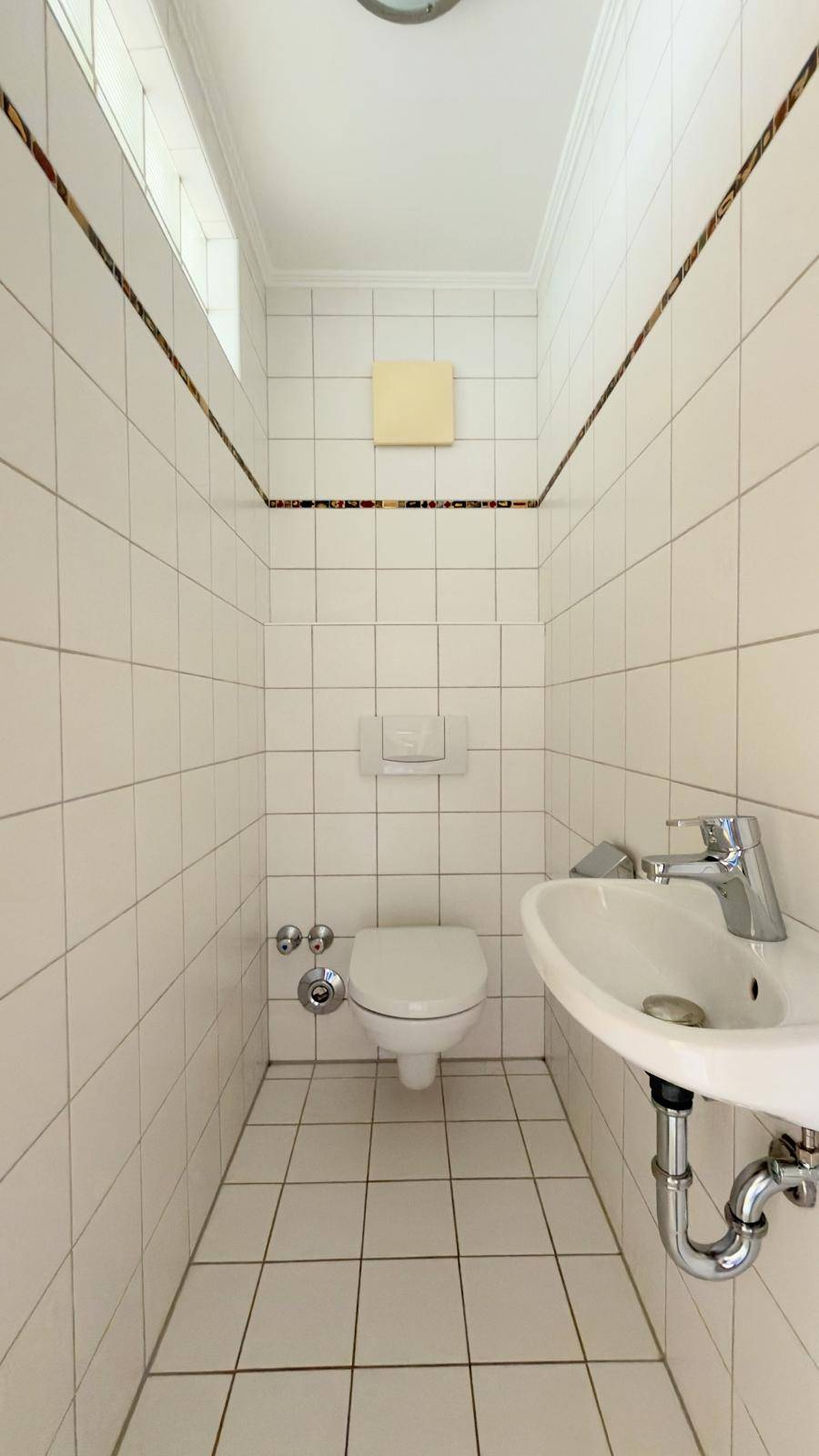 Kleines Gäste-WC mit Wand-WC, Waschbecken und Fliesen.