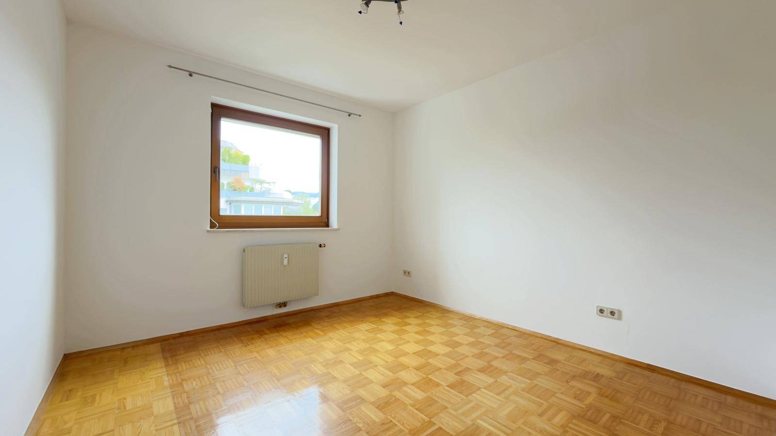 Helles Schlafzimmer mit Parkettboden und großem Fenster.