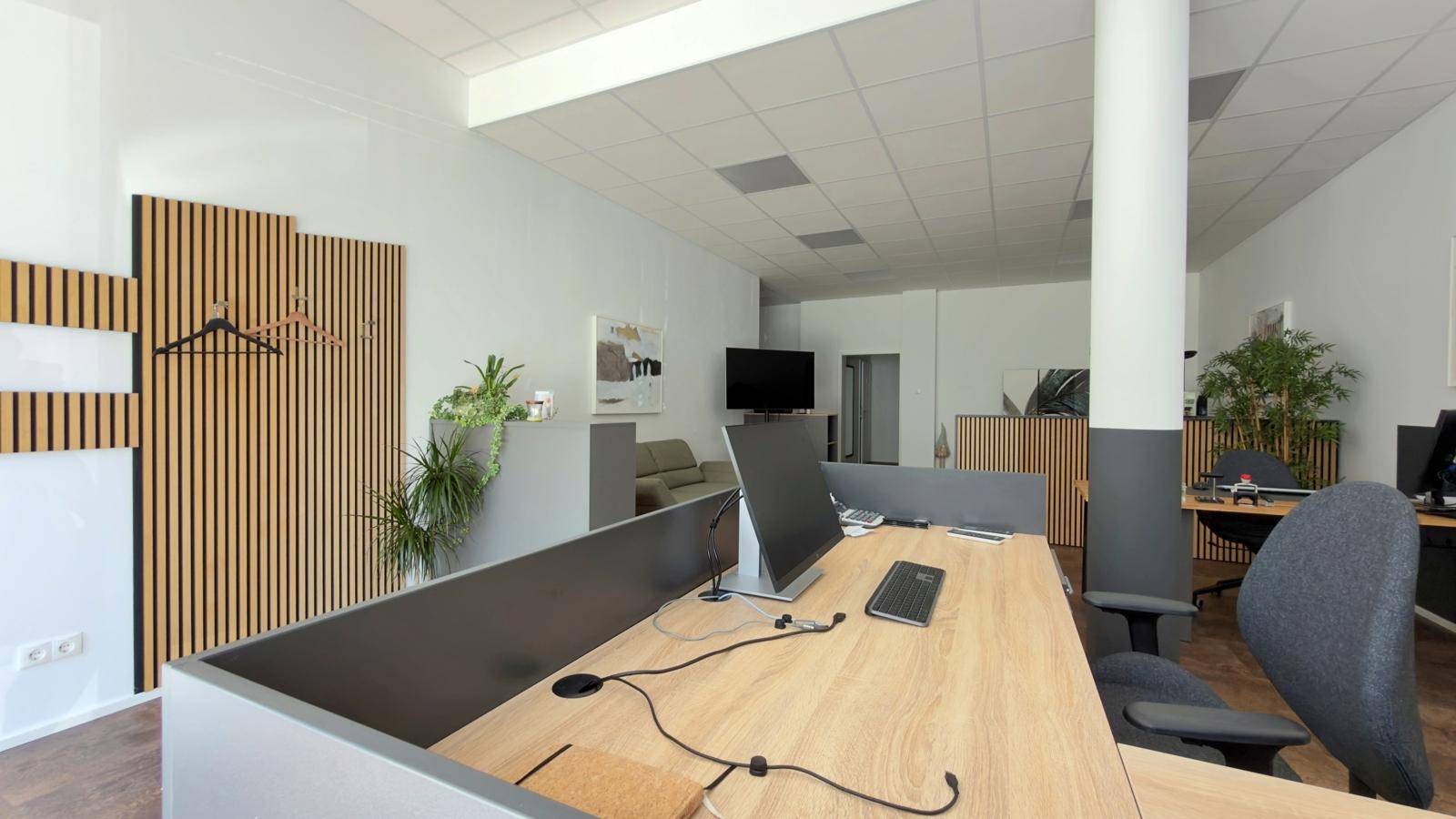 Moderner Arbeitsplatz mit Computer, Telefon und einer dekorativen Holzlamellenwand im Hintergrund.