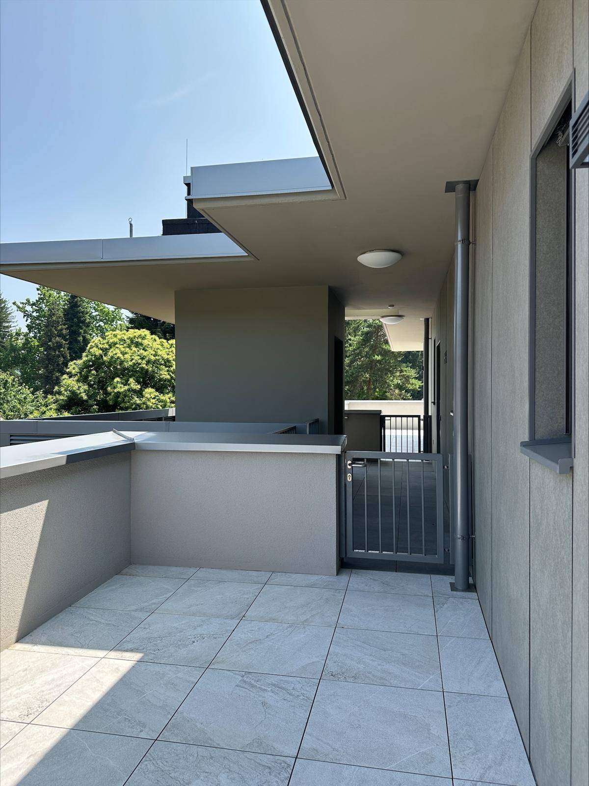 Kleinerer Balkonbereich mit Fliesenboden und einem Zugangstor, umgeben von moderner Architektur.