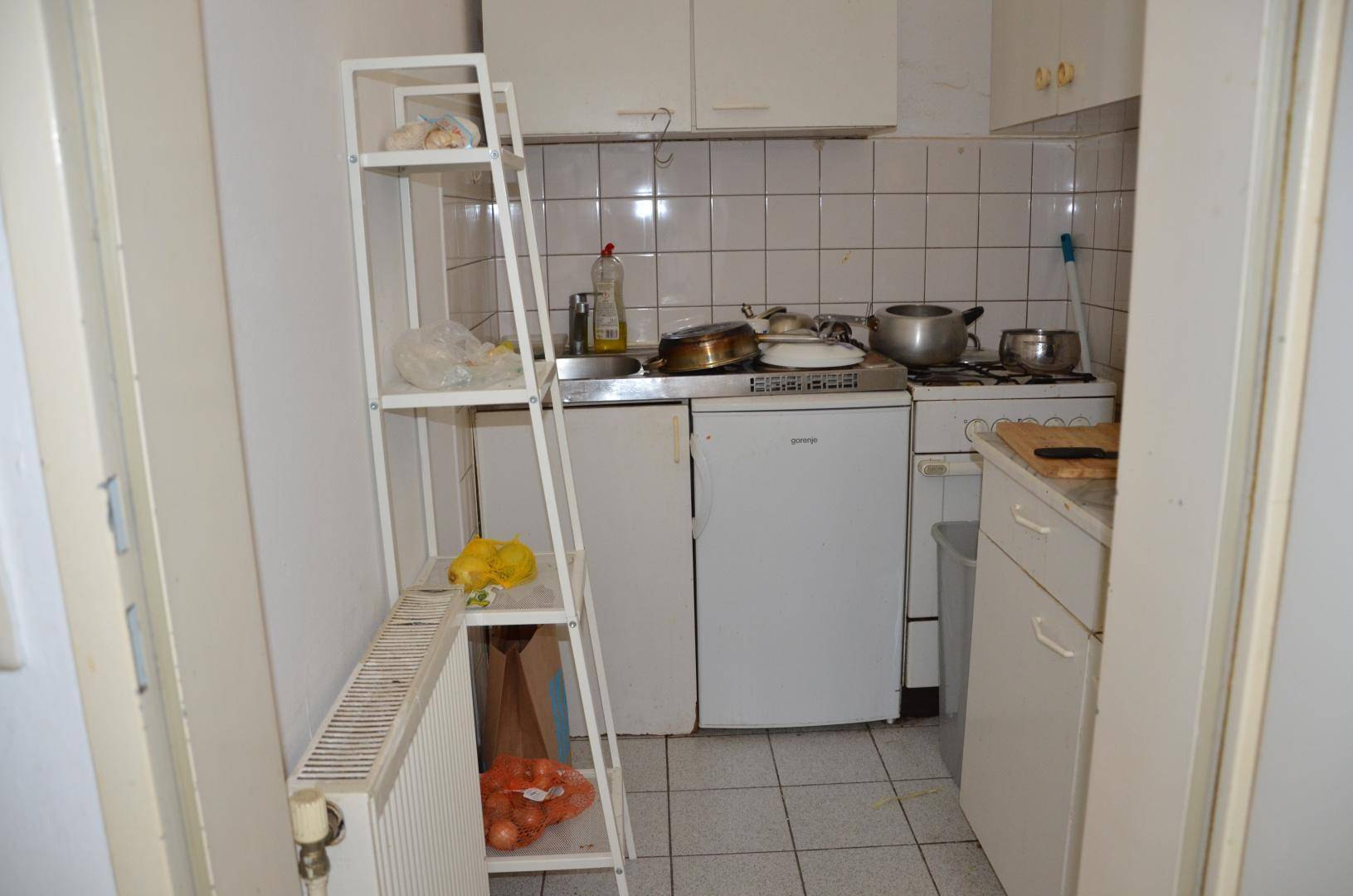 Kleine, funktionale Küchenzeile mit weißen Fliesen, Kühlschrank und grundlegenden Kochgeräten.