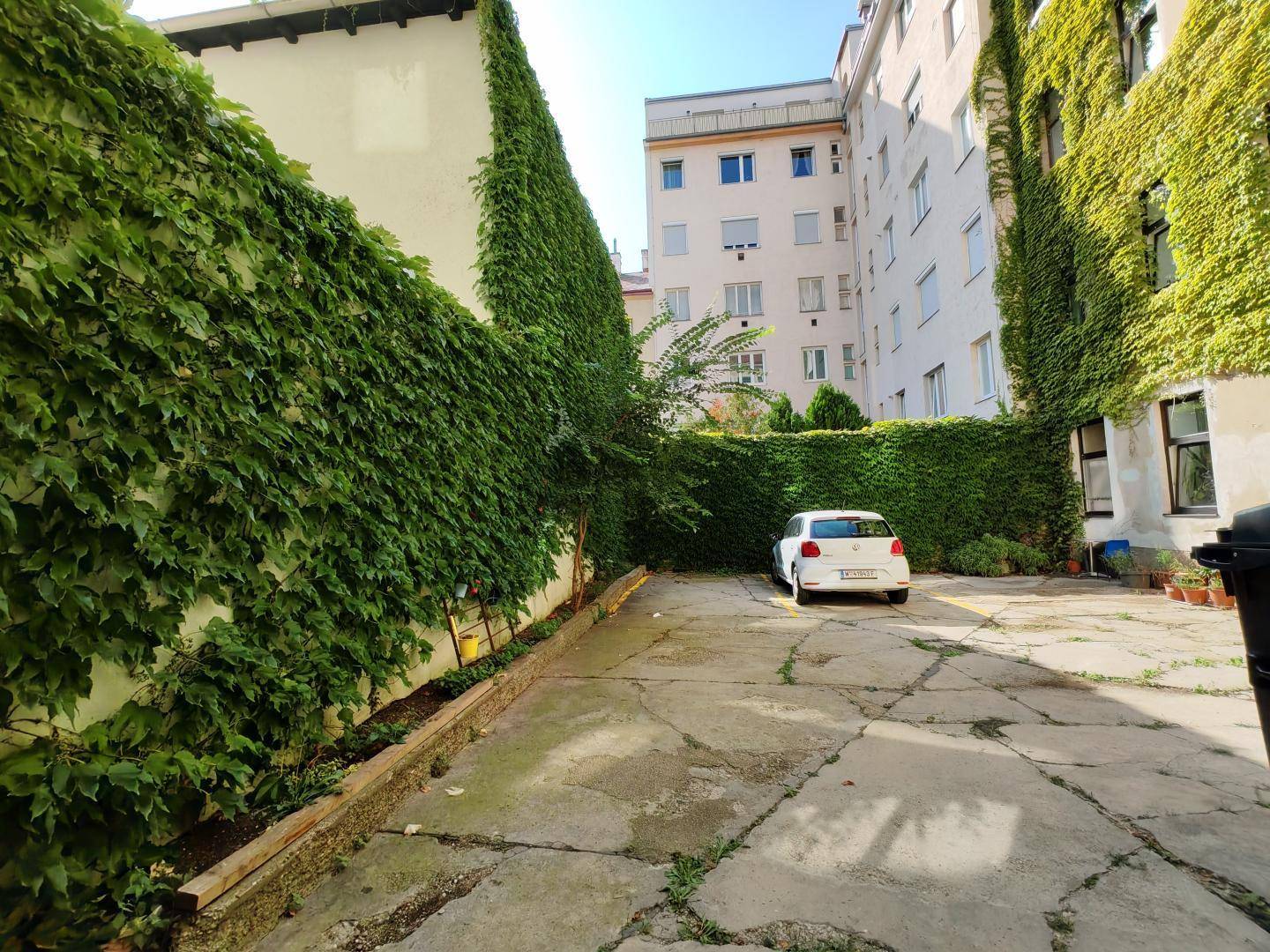 Außenparkplatz im Innenhof, umgeben von begrünten Wänden und Gebäuden, bietet Stellfläche.