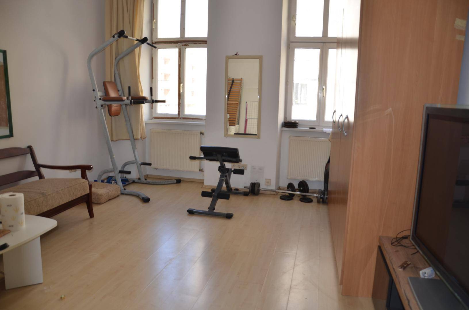 Raum mit Laminatboden, großen Fenstern und verschiedenen Fitnessgeräten für das persönliche Training.