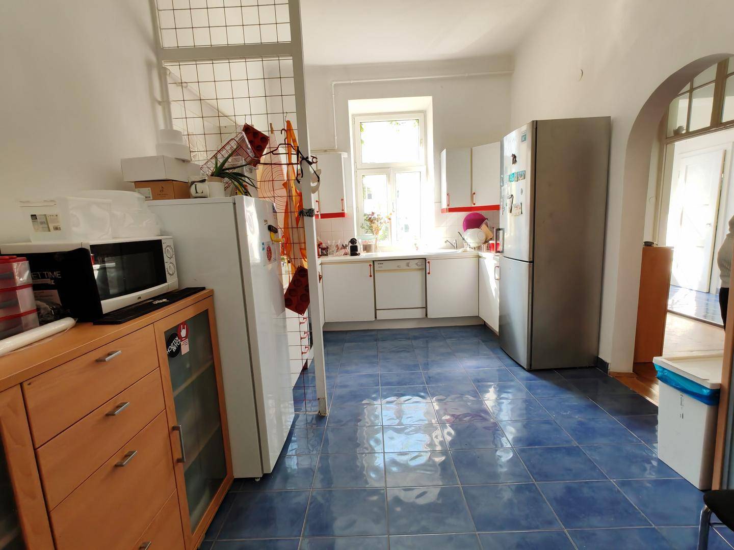 Geräumige Küche mit blauen Bodenfliesen, weißen Schränken und modernen Geräten, gut ausgestattet.
