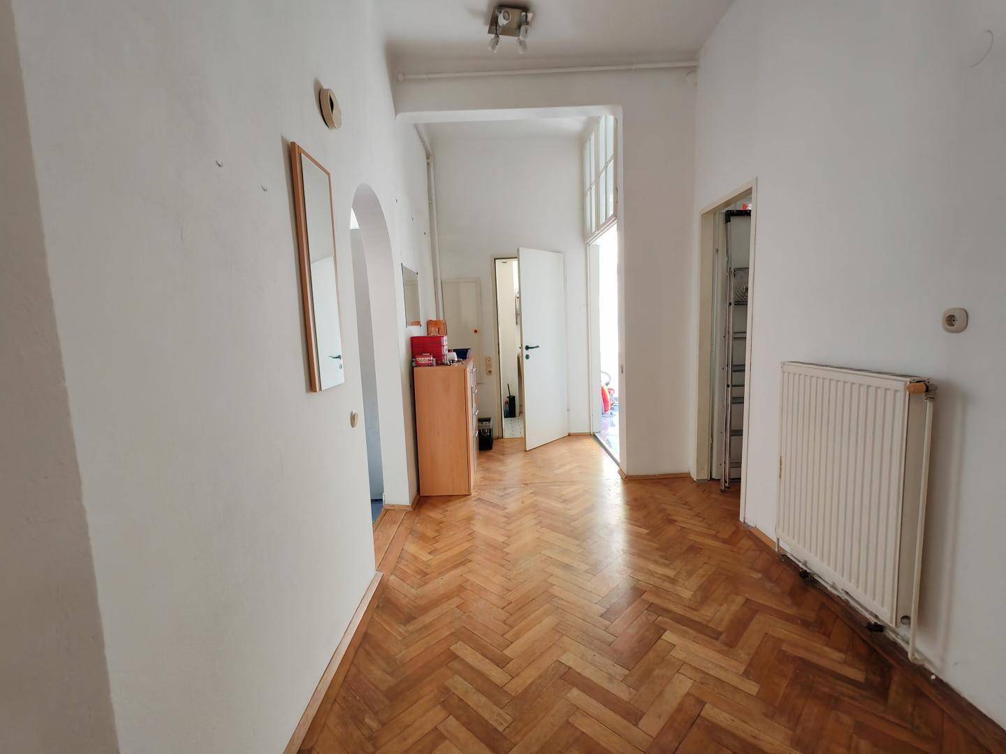 Heller Flur mit Fischgrätparkett, hohen Decken und Zugang zu verschiedenen Zimmern der Wohnung.