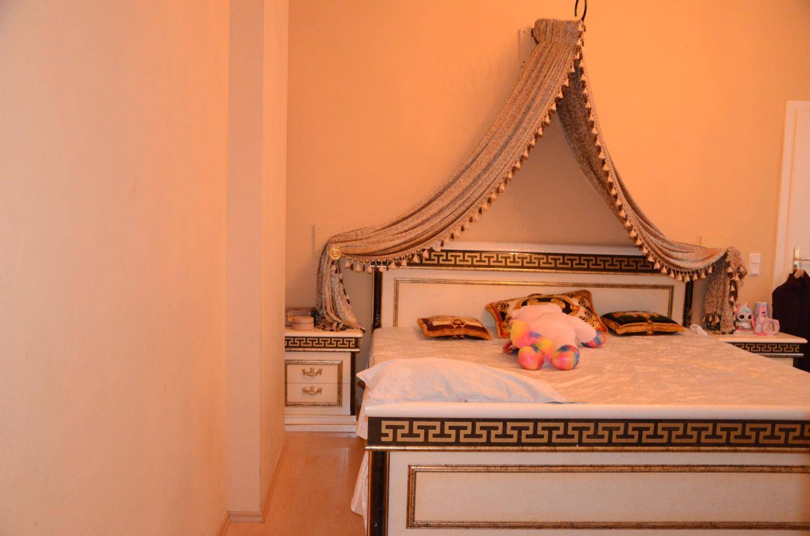 Schlafzimmer mit einem großen Bett, Baldachin und passenden Nachttischen in hellem Design und Laminatboden.