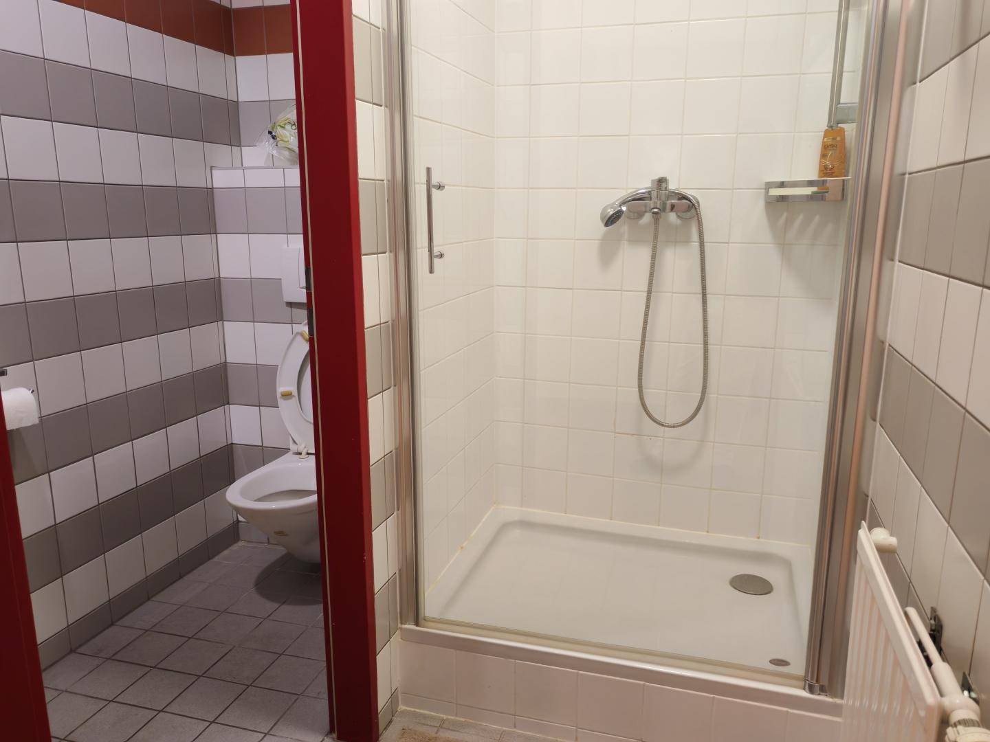 Badezimmer mit Duschkabine, gestreiften Fliesen und einer Toilette im Hintergrund, alles in gutem Zustand.
