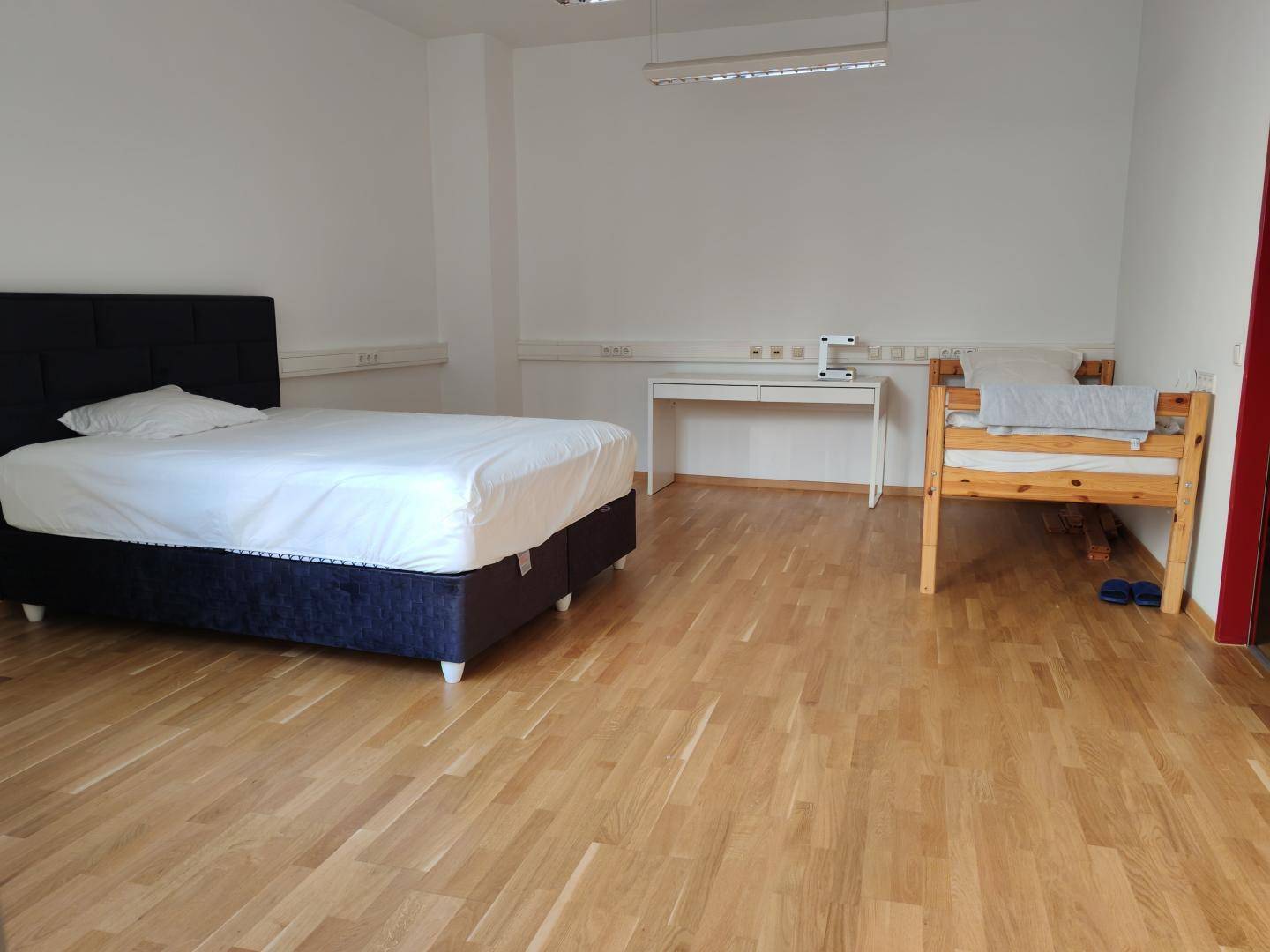 Helles Schlafzimmer mit Doppelbett, Schreibtisch und einem zusätzlichen Einzelbett, ausgestattet mit Holzfußboden.