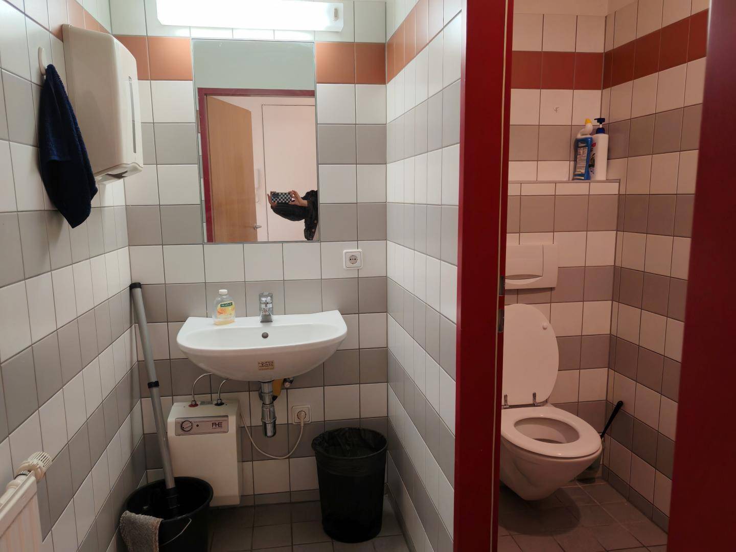 Badezimmer mit gestreiften Fliesen, Waschbecken, Toilette und einem Spender für Seife oder Desinfektionsmittel.