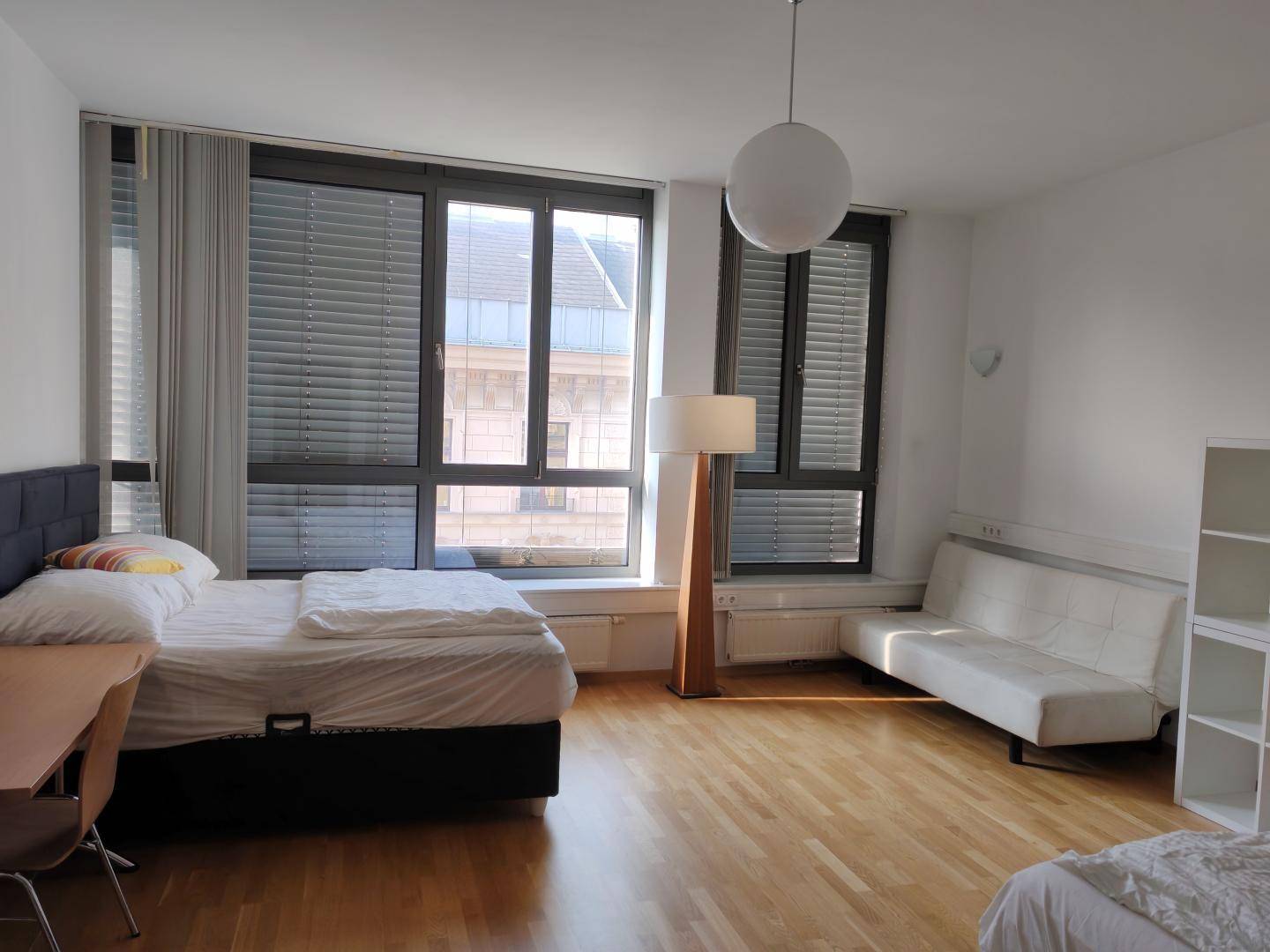 Helles Schlafzimmer mit großem Fenster, Doppelbett, Sofa und Schreibtisch, ausgestattet mit Holzfußboden.