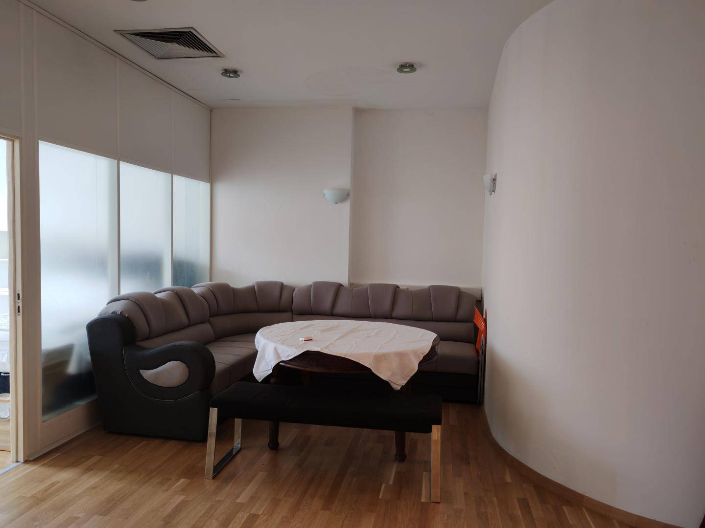 Gemütlicher Wohnbereich mit Ecksofa, rundem Tisch und Holzfußboden, beleuchtet durch Deckenstrahler.